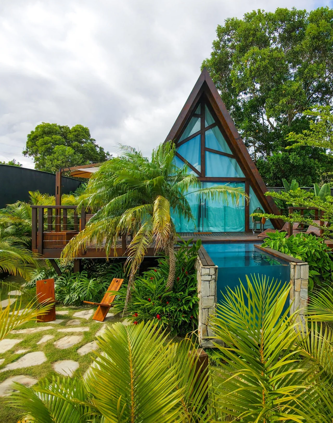 Cabana triangular, piscina e vegetação de diferentes alturas.